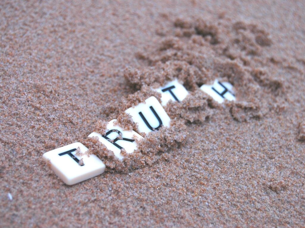 The word truth in scrabble letters being immersed with sand.